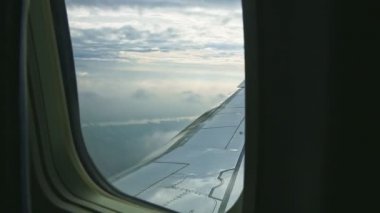 Büyük çelik kanat üzerindeki uçak penceresinden hava manzarası yumuşak beyaz bulutların üzerinde uçar.