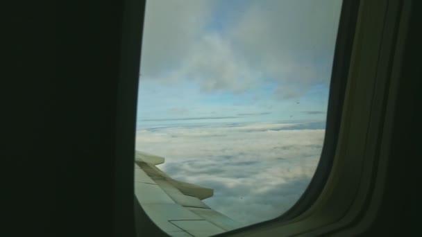 Vue aérienne à travers la fenêtre de l'avion sur des nuages blancs pelucheux volent rapidement au-dessus de l'aile en acier — Video