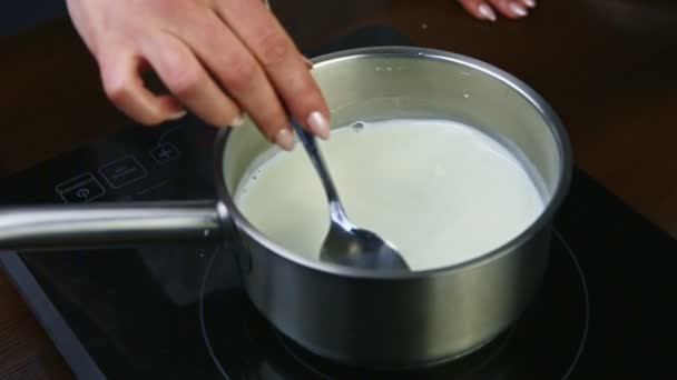 Slow motion closeup female hand by spoon stirs hot milk in metal saucepan — Stock Video