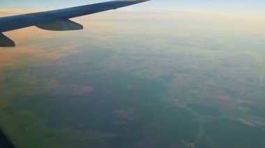 Çelik kanattaki uçak penceresinden yeşil karanın üzerinde sis ile uçuyor.