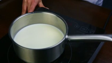 Kadın elleri sütü kaynatmak için elektrikli ocağa küçük metal tencereler koyar.