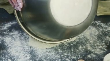 Ağır çekimde kadın elleri metal kaseden küçük yığınlara un yayıyor.