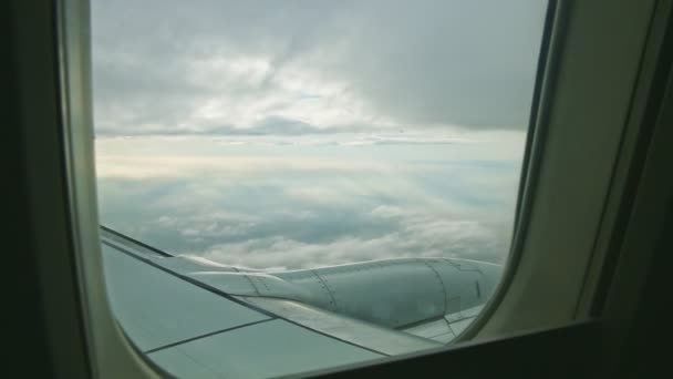 Zicht vanuit de lucht door vliegtuigraam op grote stalen vleugel vliegen boven pluizige witte wolken — Stockvideo