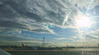 Mavi gökyüzünün altında birçok uçak silueti olan havaalanı pistinin genel manzarası