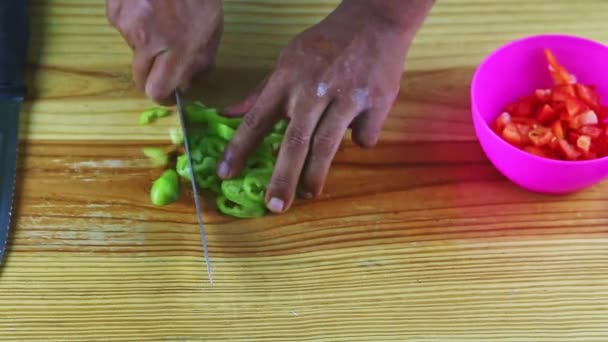 Vue de dessus sur l'homme à la peau foncée par les mains coupant des tranches de poivron vert — Video