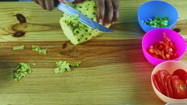 Вид зверху на людину руками за ножем очищає ананас від шкірки на дерев'яному столі — стокове відео