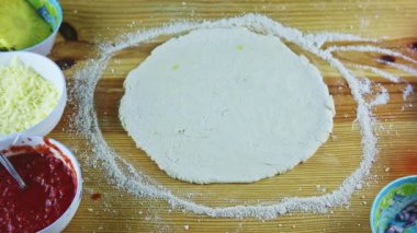 Erkek ellerine tepeden bakıldığında zeytinyağı damlaları yuvarlak pizza hamuruna damlıyor ahşap masada.
