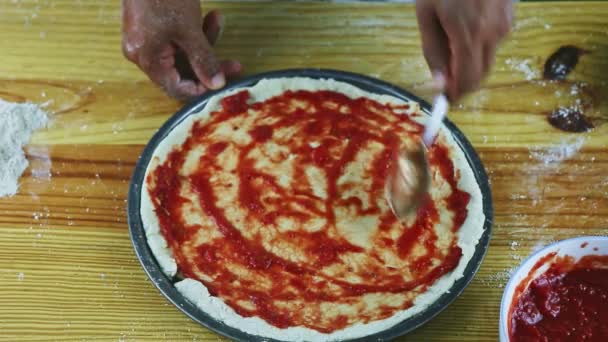 Vista dall'alto uomo primo piano mani da cucchiaio mettere salsa di pomodoro sulla pasta della pizza — Video Stock