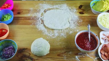 En üstteki adam elleriyle ahşap masada pizza hamuru yapıyor.