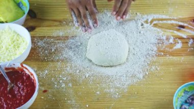 Şefin üst görüntüsü, pizza hamurunu ahşap masada döndürür.