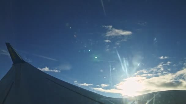 翼上の航空機の窓からの空の景色明るい太陽に対してふわふわの雲の上を飛ぶ — ストック動画