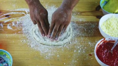 Sarı ahşap masada pizza hamuru yapan adamın üst görüntüsü.
