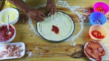 Erkeğin üst görüntüsü pizza hamurunun sınırlarını hala yuvarlak bir tabakta yapıyor.