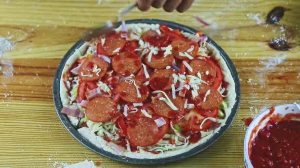Top view zbliżenie na rękach człowieka umieścić sos pomidorowy na surowe pizzy z pepperoni — Wideo stockowe