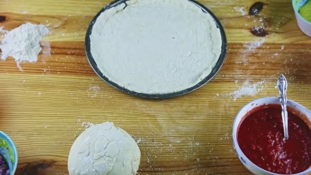 Widok z góry powiększyć z okrągłego naczynia do pieczenia z ciasta pizzy walcowane na drewnianym stole — Wideo stockowe