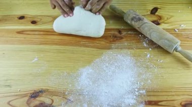 Koyu tenli adamın üst görüntüsü ahşap masada beyaz hamuru elle yoğurur.