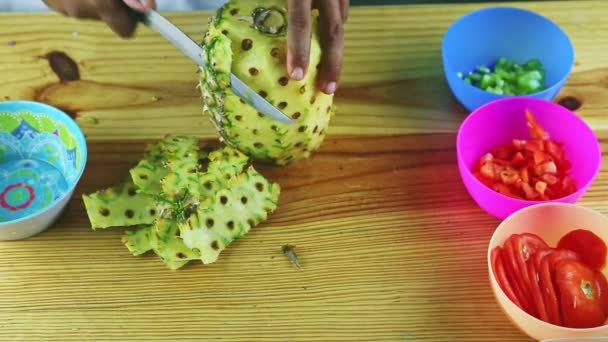 Bovenaanzicht op mensenhanden door mes reinigt ananas van schil op houten tafel — Stockvideo