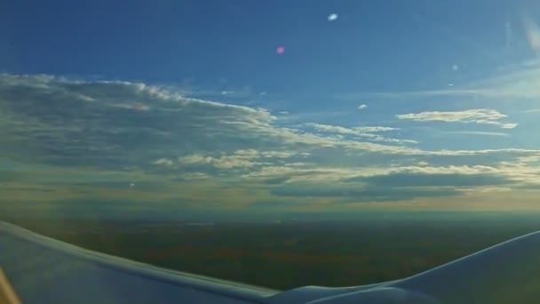 밝은 태양을 배경으로 솜털 구름 위를 날아가는 강철 날개 위의 비행기 창문에서 찍은 공중 사진 — 비디오