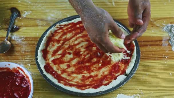 Top view närbild man händer sätta riven ost på rå pizza med tomatsås — Stockvideo