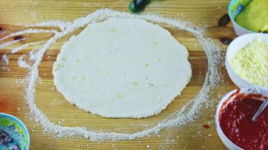 Erkek ellerine üstten bakıldığında zeytinyağı damlaları yuvarlak pizza hamurunun üzerine konur.