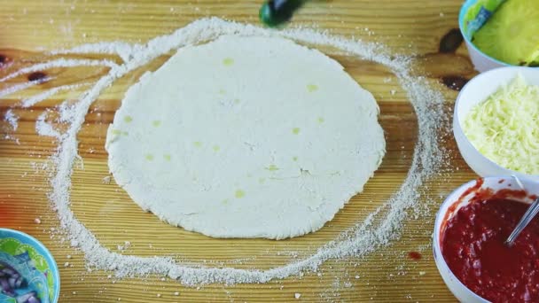 Vista dall'alto sulle mani dell'uomo mettere gocce di olio d'oliva su pasta rotonda pizza sul tavolo di legno — Video Stock