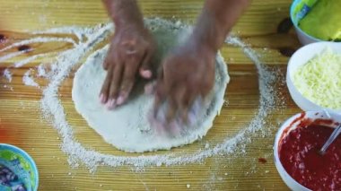 Üst kattaki yakın plan adam elle pizza hamurunu ahşap masada ince ve yuvarlak yapar.