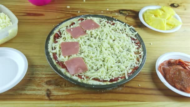 Top view closeup man by hands puts ham pieces on raw pizza with different ingredients — Stock Video