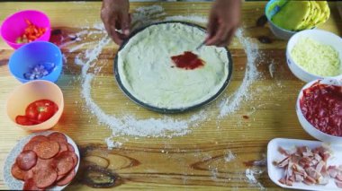 Erkeğin ellerine kaşıkla yukarıdan bak. Yarı bitmiş pizzaya domates sosu koy.