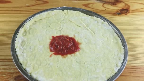 Widok z góry powiększ z okrągłego ciasta pizzowego z sosem pomidorowym na drewnianym stole — Wideo stockowe