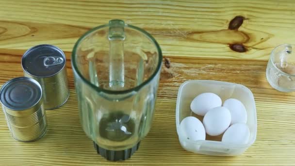木製のテーブルの上からは、空のブレンダー、白い卵、スチール缶が現れ — ストック動画