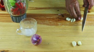 Bıçakla kesilen insan ellerinin üst görüntüsü ahşap masadaki sarımsak parçalarını temizler.