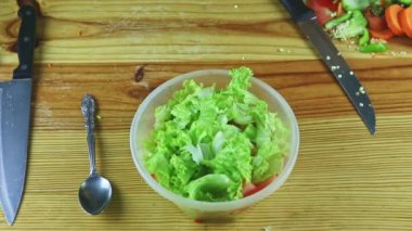 Büyük plastik kasede salataya kesilmiş sebzeleri kaşık kaşık ile insan ellerinin üst görüntüsü.