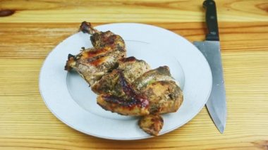 Üst manzara, fırında pişirilmiş otların yarısında tavuk beyaz tabakta bıçakla servis edilir.