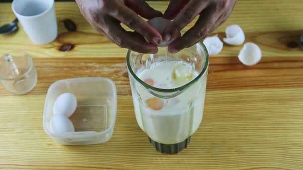 Bovenaanzicht op mens door handen rem twee kippeneieren in blender kelk met melk — Stockvideo