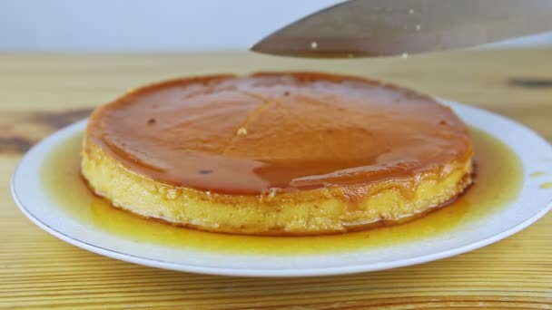 Slowly zoom in on man hands by knife slice soft milk flan with caramel sauce on plate — Stock Video