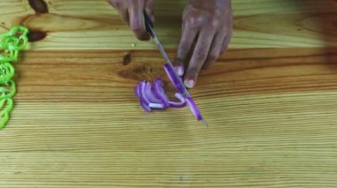 Koyu tenli adamın üst görüntüsü. Elleri bıçakla kesilmiş. Büyük mor soğanın yarısı.