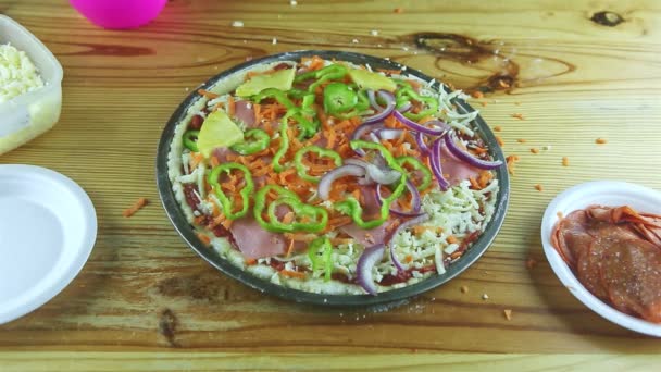Bovenaanzicht op mensenhanden zet ananas plakjes op rauwe pizza met verschillende ingrediënten — Stockvideo