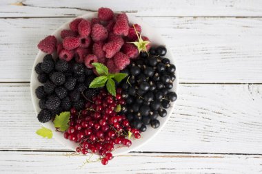 Kırmızı ve siyah kuş üzümü ve ahududu ve nane, yararlı olgun çilek bir tabakta ahşap arka plan beyaz