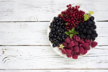 Kırmızı ve siyah kuş üzümü ve ahududu ve nane, yararlı olgun çilek bir tabakta ahşap arka plan beyaz