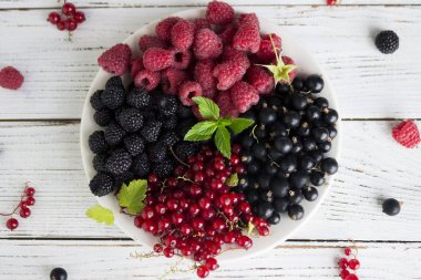 Kırmızı ve siyah kuş üzümü ve ahududu ve nane, ahşap bir plaka üzerinde yararlı olgun çilek adam beyaz