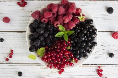 Kırmızı ve siyah kuş üzümü ve ahududu ve nane, ahşap bir plaka üzerinde yararlı olgun çilek adam beyaz