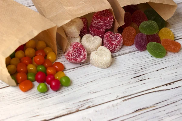 Round colored candy and marmalade in a paper bag on a wooden table, bright sweets, white background