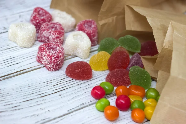 Round colored candy and marmalade in a paper bag on a wooden table, bright sweets, white background