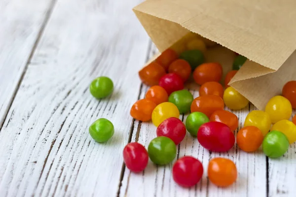 Round colored candy in a paper bag on a wooden table, bright sweets, backgroun