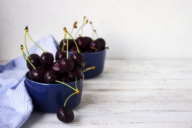 Olgun kiraz ahşap beyaz arka plan, sağlıklı meyve üzerinde koyu mavi tabak içinde