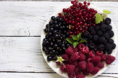 Siyah ve kırmızı kuş üzümü, bir plaka bir yaprak ahududu, beyaz arka plan üzerinde siyah ve kırmızı ahududu