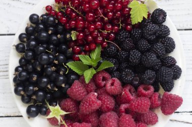 Siyah ve kırmızı kuş üzümü, bir plaka bir yaprak ahududu, beyaz arka plan üzerinde siyah ve kırmızı ahududu