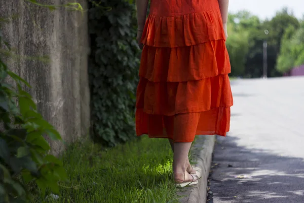 Beautiful woman in orange linen dress with ruffles, summer style, fashion. The girl is on the curb bac