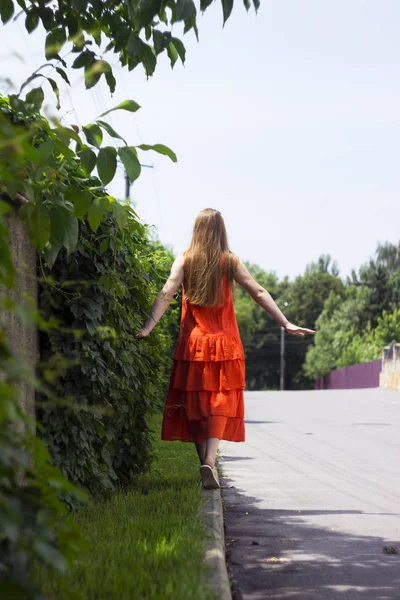 Beautiful woman in orange linen dress with ruffles, summer style, fashion. The girl is on the curb back