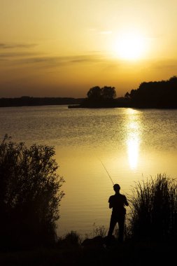 Genç bir adam gün batımında gölde balık yakalar. Güzel güneş yeniden